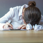 Writer with head down and crumpled drafts.