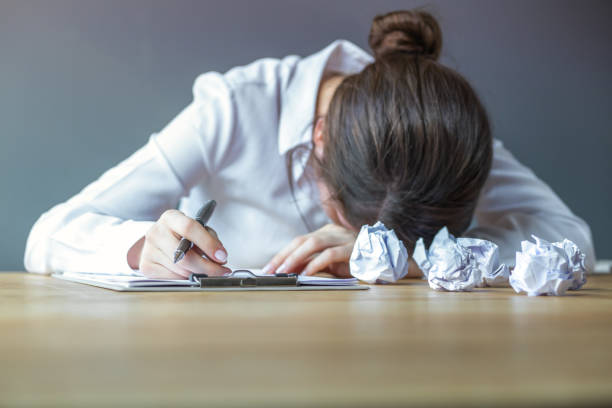 Writer with head down and crumpled drafts.